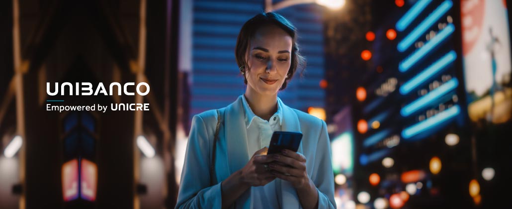 Mulher sorridente à noite na rua, ao telemóvel, com a app da Unibanco.